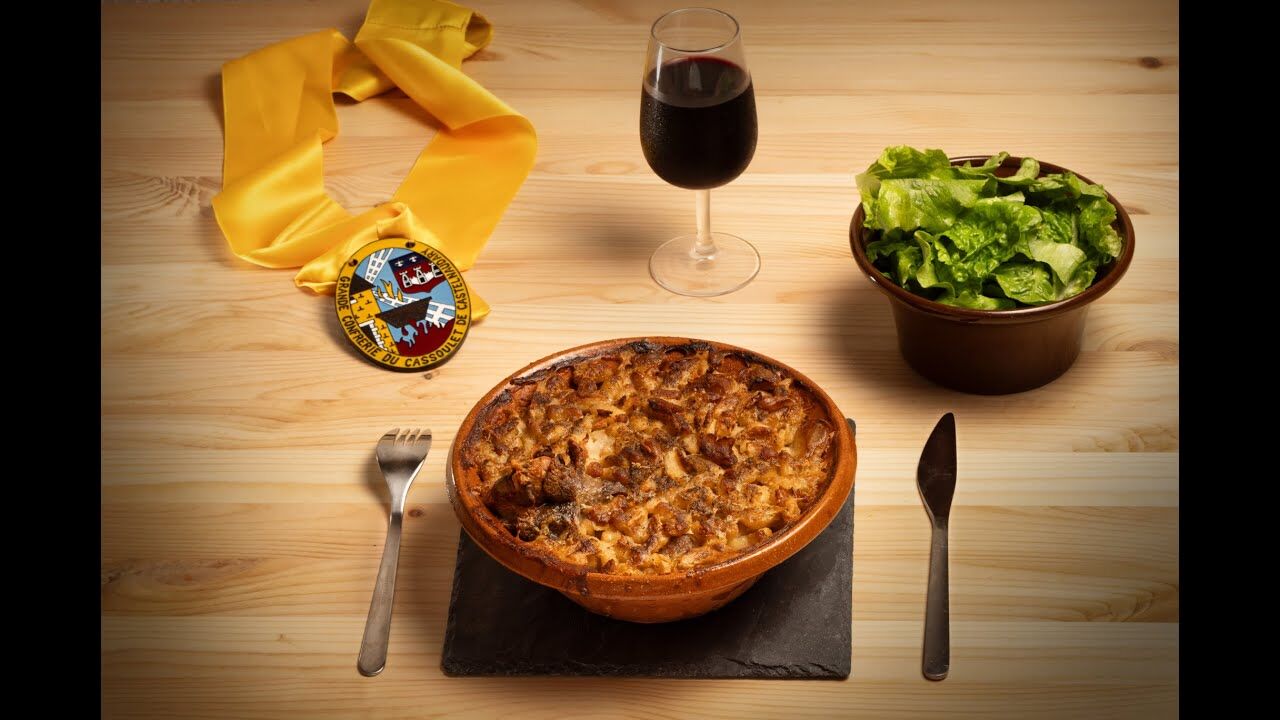 Cassoulet served in an earthenware cassole, a glass of red wine and a sash from the Grande Confrérie du Cassoulet de Castelnaudary